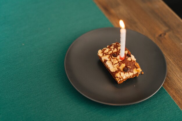 Gâteau en gros plan avec une bougie allumée dans la pièce lumineuse sur une assiette sombre, pas de monde.