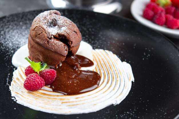 Gâteau de lave au pouding au chocolat avec crème à la vanille, framboise et menthe sur une plaque noire