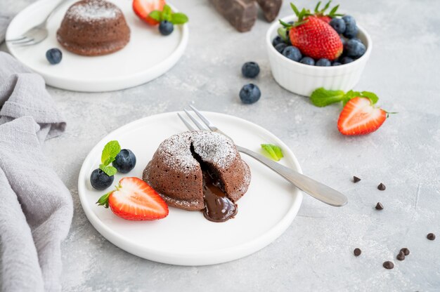 Gâteau de lave fondant au chocolat avec des baies fraîches sur une assiette sur fond gris.