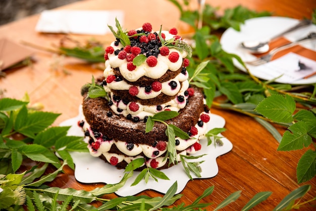 Un gâteau de mariage aux fruits rouges servi à l'extérieur. Couverts en arrière-plan.