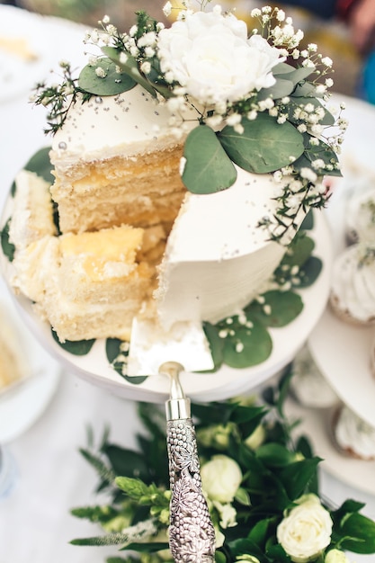 Gâteau de mariage blanc coupé décoré de feuilles vertes et de fleurs de gypsophile.