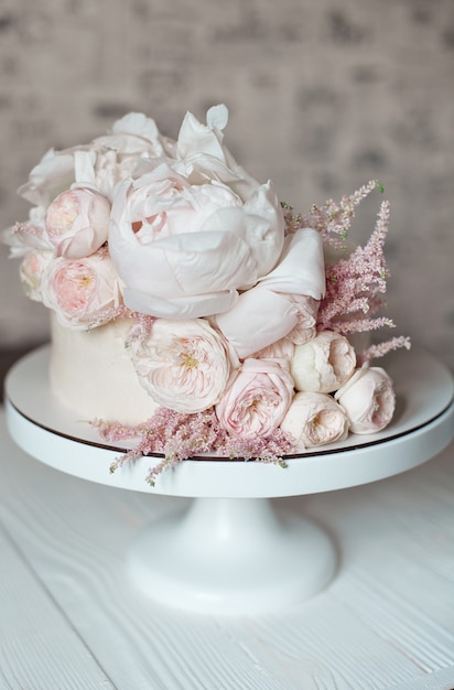 Gâteau de mariage blanc décoré de roses fraîches, de pivoines et de verdure