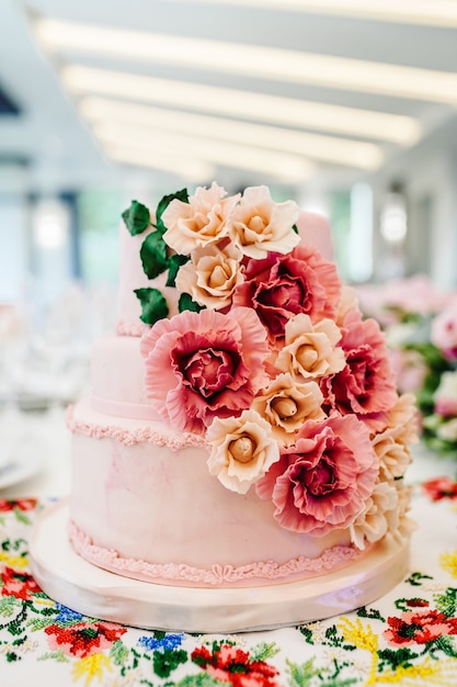 Gâteau de mariage blanc avec des fleurs roses et des verts sur une table de fête avec de la pâtisserie. gros plan du gâteau. Table douce.