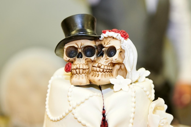 Gâteau de mariage blanc avec une tête de mort et des roses rouges la mariée et le marié sous la forme d'un squelette