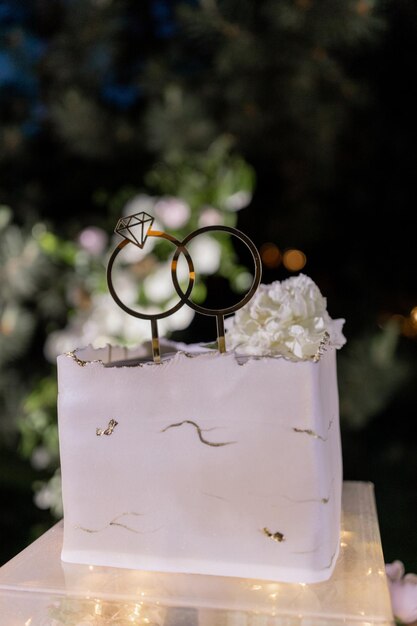 Photo un gâteau de mariage élégant étagé éclairé de lumières romantiques sur une toile de fond florale en plein air