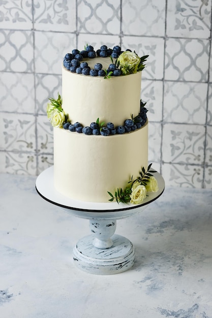 Un gâteau de mariage grand et élégant. Un gâteau à deux étages pour de belles vacances. Gâteau blanc décoré de bleuets frais et de roses blanches.