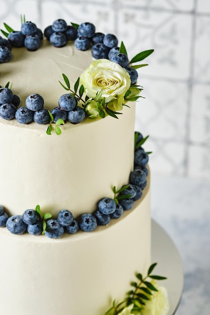 Un gâteau de mariage grand et élégant. Un gâteau à deux étages pour de belles vacances. Gâteau blanc décoré de bleuets frais et de roses blanches.