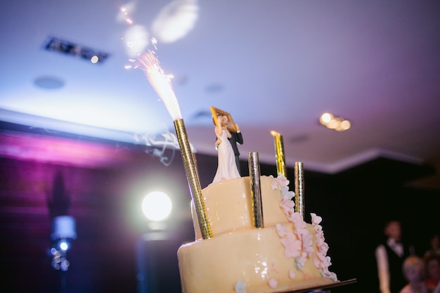 Un gâteau de mariage avec pyrotechnie. Les mariés coupent un morceau de gâteau avec un couteau. Photo en gros plan.