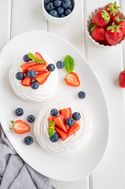 Gâteau de meringue Pavlova avec crème fouettée et baies fraîches sur le dessus sur une assiette sur un fond en bois blanc. Dessert d'été. Espace de copie, vue de dessus.