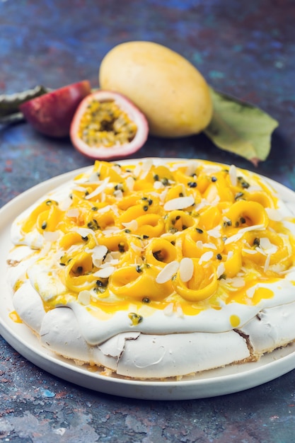 Gâteau meringué Pavlova à la mangue fraîche et aux fruits de la passion et crème fouettée sur fond d'ardoise, de pierre ou de béton