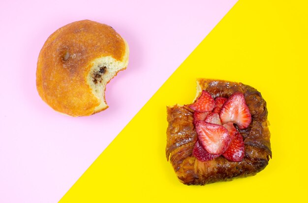 Gâteau mordu et beignet. Tentation de délicieux bonbons et desserts sur fond rose et jaune. Minimalisme, image originale et créative. Beau fond d'écran de nourriture.