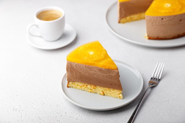 Photo gâteau à la mousse au chocolat et à l'orange avec de la gelée à base de biscuits et des cercles d'orange un morceau de gâteau au fromage fait maison et une tasse de café dessert traditionnel de vacances close-up sélectif