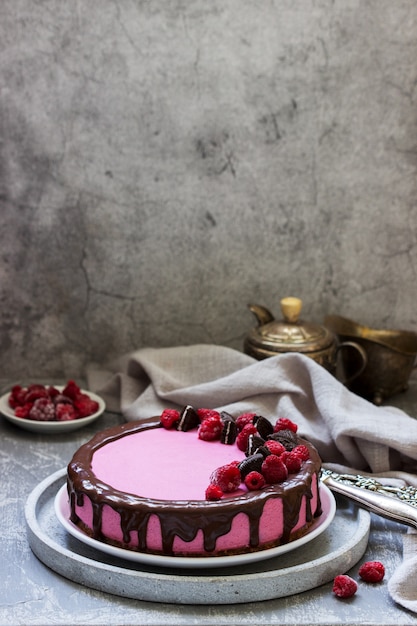 Gâteau mousse aux groseilles décoré de morceaux de biscuits oreo et de framboises.