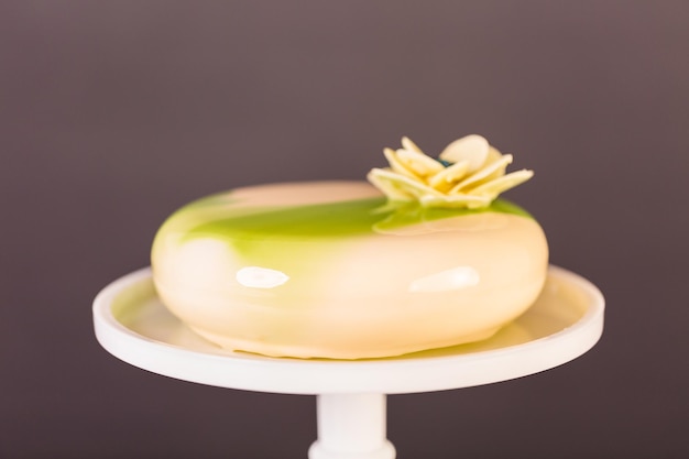 Gâteau mousse gourmand avec glaçage miroir blanc et vert décoré de fleur de chocolat blanc.