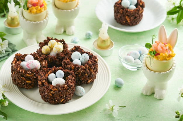 Gâteau nid de chocolat de Pâques avec mini œufs de bonbons au chocolat avec fleurs de cerisier ou de pomme en fleurs sur table de fond vert Recette créative pour table de Pâques avec décorations de vacances Vue de dessus