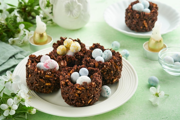 Gâteau nid de chocolat de Pâques avec mini œufs de bonbons au chocolat avec fleurs de cerisier ou de pomme en fleurs sur table de fond vert Recette créative pour table de Pâques avec décorations de vacances Vue de dessus