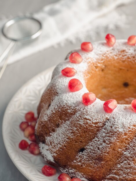 Gâteau de Noël en forme de couronne avec du sucre en poudre et des graines de grenade sur une plaque blanche