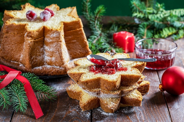 Gâteau de Noël italien Pandoro coupé en tranches sur une table en bois avec décor de Noël et confiture de fruits