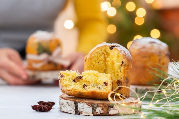 Un gâteau de Noël italien traditionnel panettone sur une table rustique des mains féminines tiennent le gâteau