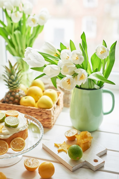 Gâteau nu aux citrons et limes, macarons sucrés et fleurs dans un vase