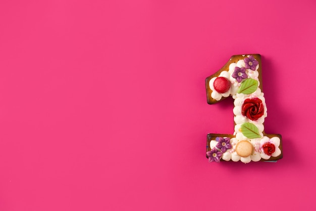 Gâteau numéro un décoré de fleurs et de biscuits sur la surface rose Espace copie