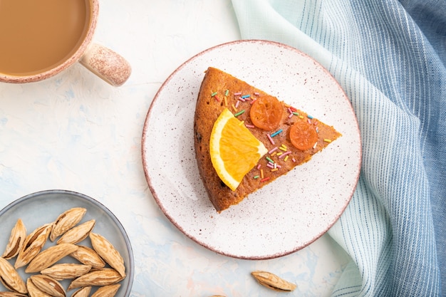 Gâteau orange aux amandes et une tasse de café sur fond de béton blanc et textile en lin bleu.