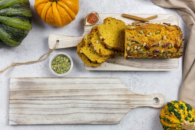 Gâteau de pain à la citrouille sur une planche à découper en bois avec des pacanes et des graines de citrouille sur un fond clair avec des citrouilles et des figues