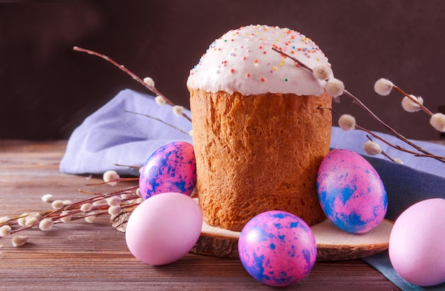 Gâteau de Pâques avec des brindilles de saule et des oeufs rose, lilas sur une surface sombre