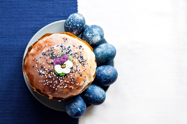 Gâteau De Pâques Décoré De Fleur De Sucre Et D'oeufs De Couleur Bleue Sur Une Plaque Sur Une Surface En Tissu Blanc Et Bleu