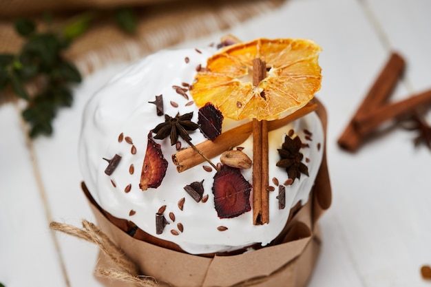 Gâteau de Pâques décoré de fruits secs et de bâtons de cannelle sur fond de bois blanc, Kulich traditionnel, Paska prêt pour la célébration