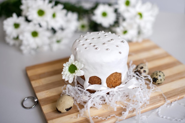 Le gâteau de Pâques en glaçure avec un ruban se dresse sur une planche avec des œufs de caille et des fleurs blanches