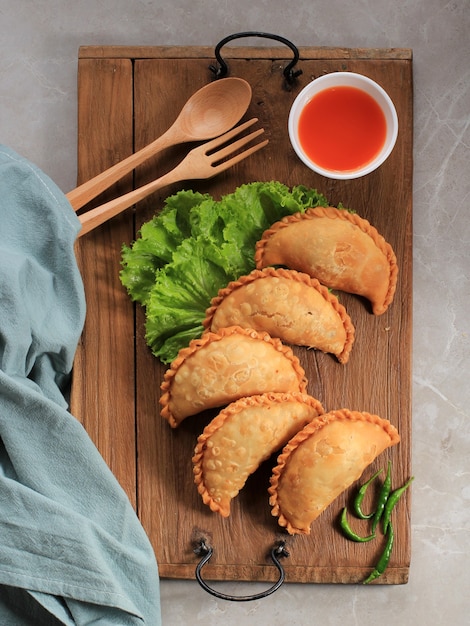 Gâteau Pastel indonésien servi sur une assiette blanche accompagné de thé. Populaire comme Curry Puff (Karipap) ou Jalangkote Makasar.