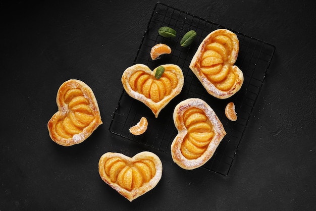 Gâteau de pâte feuilletée en forme de coeur avec des tranches de mandarine et des feuilles de menthe sur une table sombre v