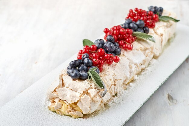 gâteau pavlova dessert meringué avec des baies fraîches sur le dessus sur une surface en bois clair.