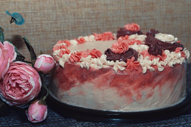 Gâteau rose avec des fleurs crème sur fond sombre