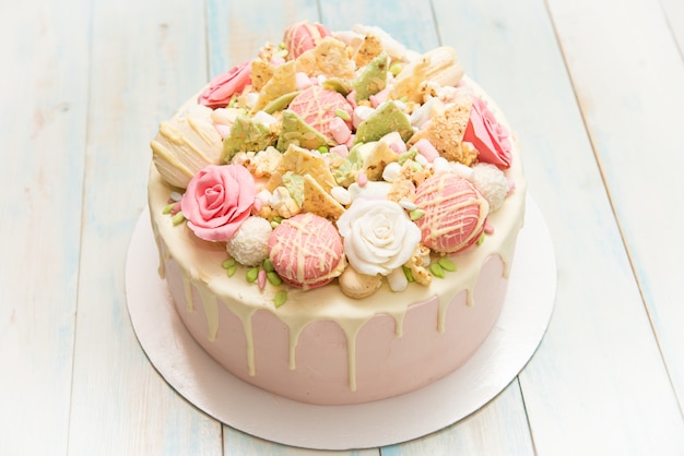 Gâteau rose avec des fleurs et des petits gâteaux sur une plaque blanche