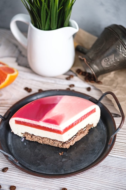 Gâteau rouge et blanc fourré à l'orange. A proximité sur une table noire se trouvent des ingrédients oranges, noix. Style rustique.