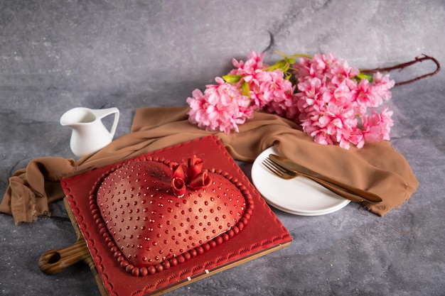 Gâteau rouge en forme de coeur avec couteau et fourchette à fleurs roses servi à bord isolé sur une serviette vue latérale des aliments cuits au café