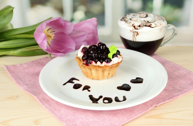 Gâteau sucré avec sauce aux mûres et au chocolat sur une assiette avec du café sur fond clair