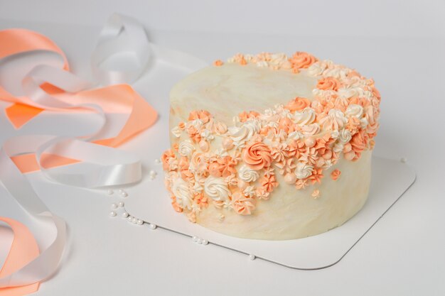 Gâteau à la vanille avec décoration de fleurs crème et rubans.