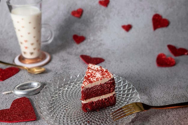 gâteau de velours rouge avec coeurs rouges et verre de lait sur fond gris pierre avec couverts en or