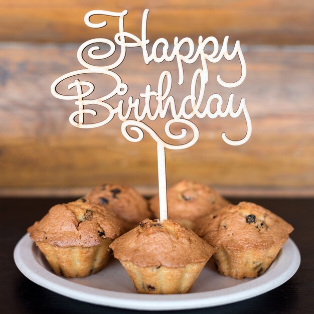 Gâteaux d'anniversaire et muffins avec panneau de voeux en bois sur mur rustique. Chante en bois avec des lettres Joyeux anniversaire et bonbons de vacances.