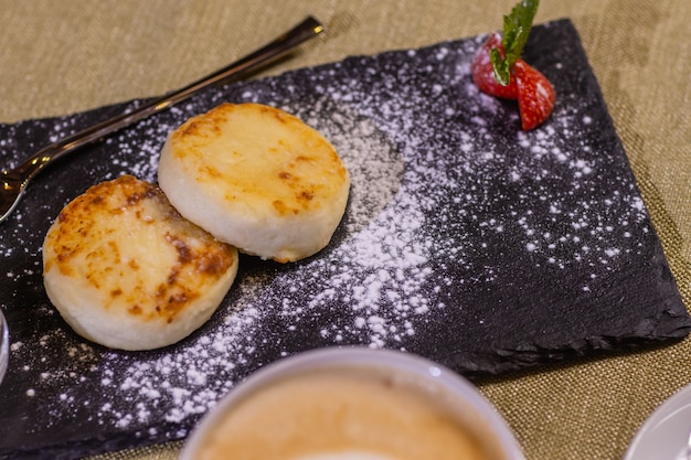 Gâteaux au fromage aux fraises. Deux caillés frits sur un plateau noir. Fermer.