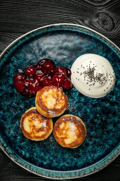 Photo gâteaux au fromage avec confiture de cerises à la crème sure sur une table en bois sombre