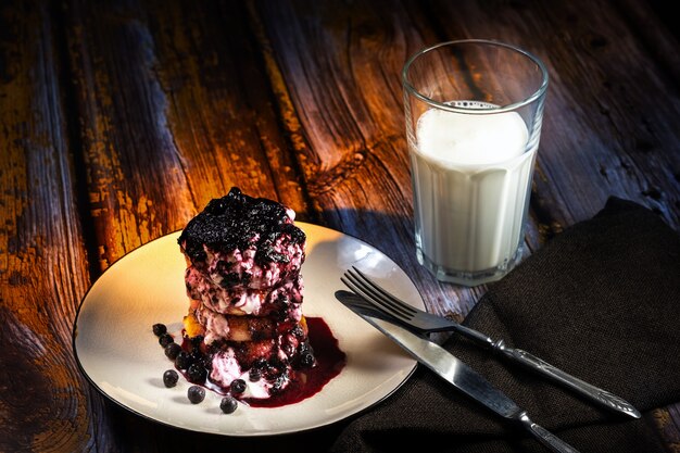 Gâteaux au fromage avec confiture de myrtilles et crème sure sur une assiette avec un verre de lait sur la table