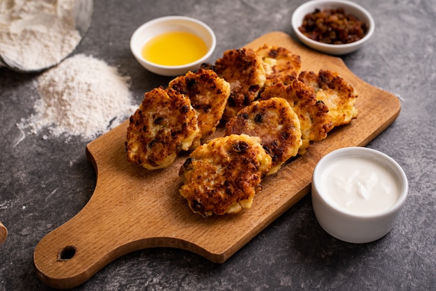 Gâteaux au fromage faits maison sur une planche avec des raisins secs et de la crème sure. Nourriture saine. Vue de dessus.