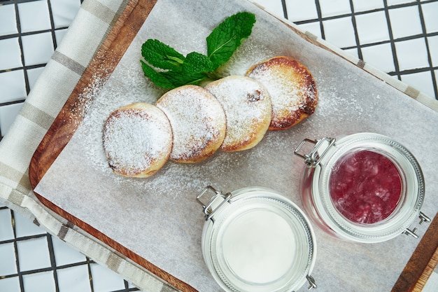 Gâteaux au fromage faits maison ou Syrniki avec de la confiture, des fruits frais et de la crème sure sur un papier kraft sur une surface blanche. Cuisine ukrainienne. Nourriture du petit déjeuner