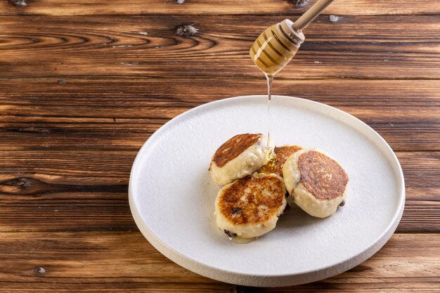 Gâteaux au fromage sur une plaque blanche avec du miel sur fond de bois.