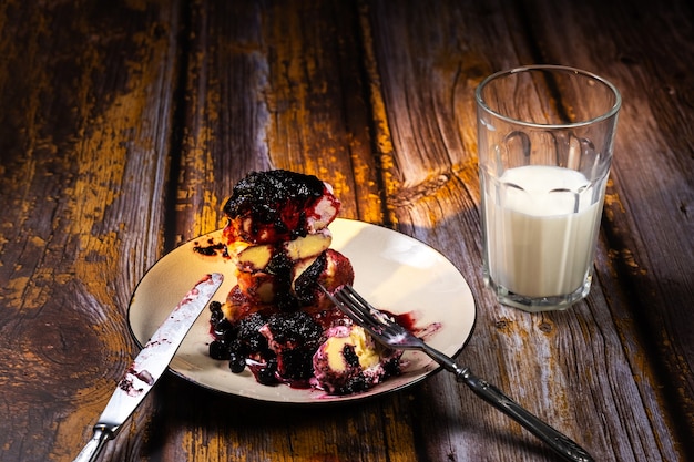 Gâteaux Au Fromage En Tranches Avec Confiture De Myrtilles Et Crème Sure Sur Une Assiette Et Un Verre De Lait Sur Une Table En Bois