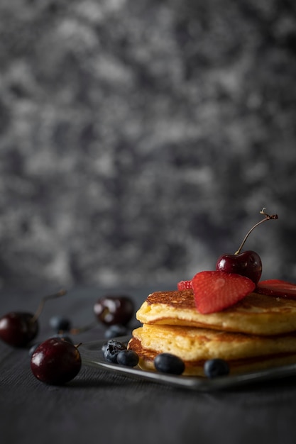 Gâteaux chauds empilés avec des fraises de cerises et des myrtilles sur une table en bois noire de cru